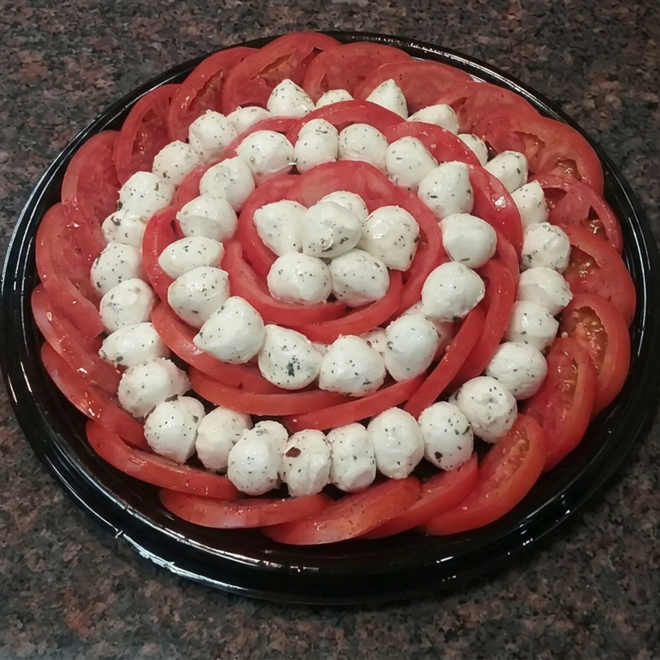 Sliced tomatoes and herb-seasoned mozzarella balls arranged in concentric circles on a black platter.